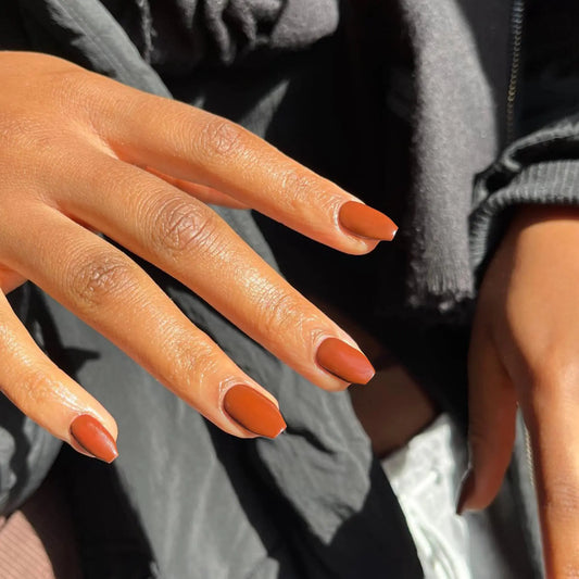 Close-up of hands with orange nail polish wearing a gray sweater.