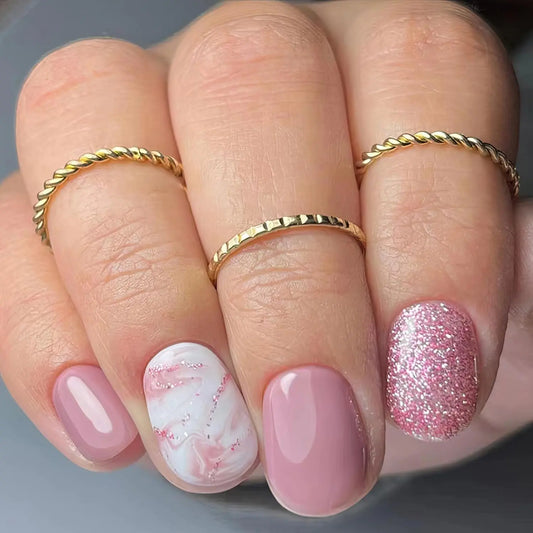 Close-up of a hand with pink and marbleized nails wearing gold rings on a gray background