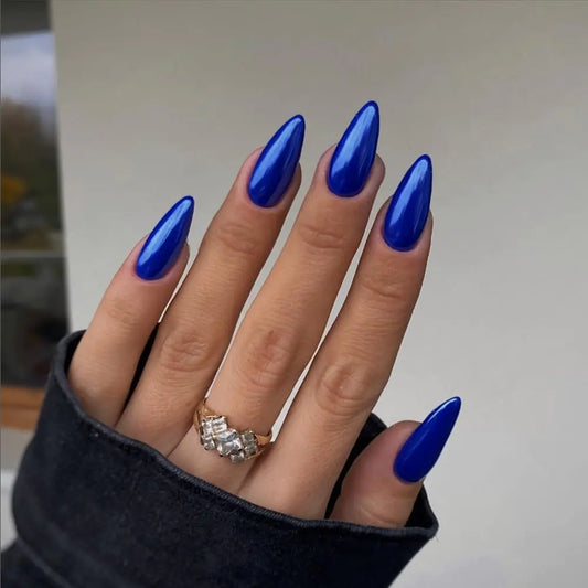Hand with blue nail polish wearing a black sleeve and diamond ring on a neutral background