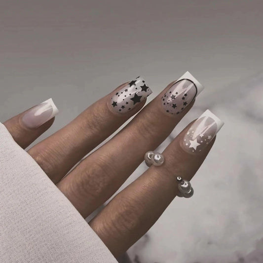 Hand with stylish nails featuring star and dot patterns on a neutral background